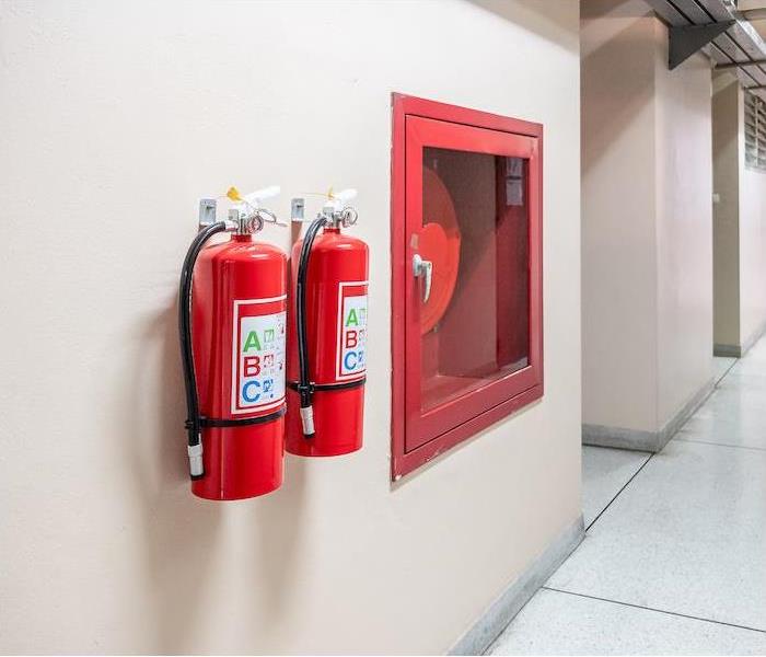 two fire extinguishers and red fire hose hanging on interior wall